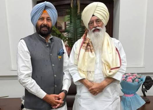 Kewal Singh Dhillon standing beside a senior Sikh public figure at an indoor meeting, with a bouquet on the desk
